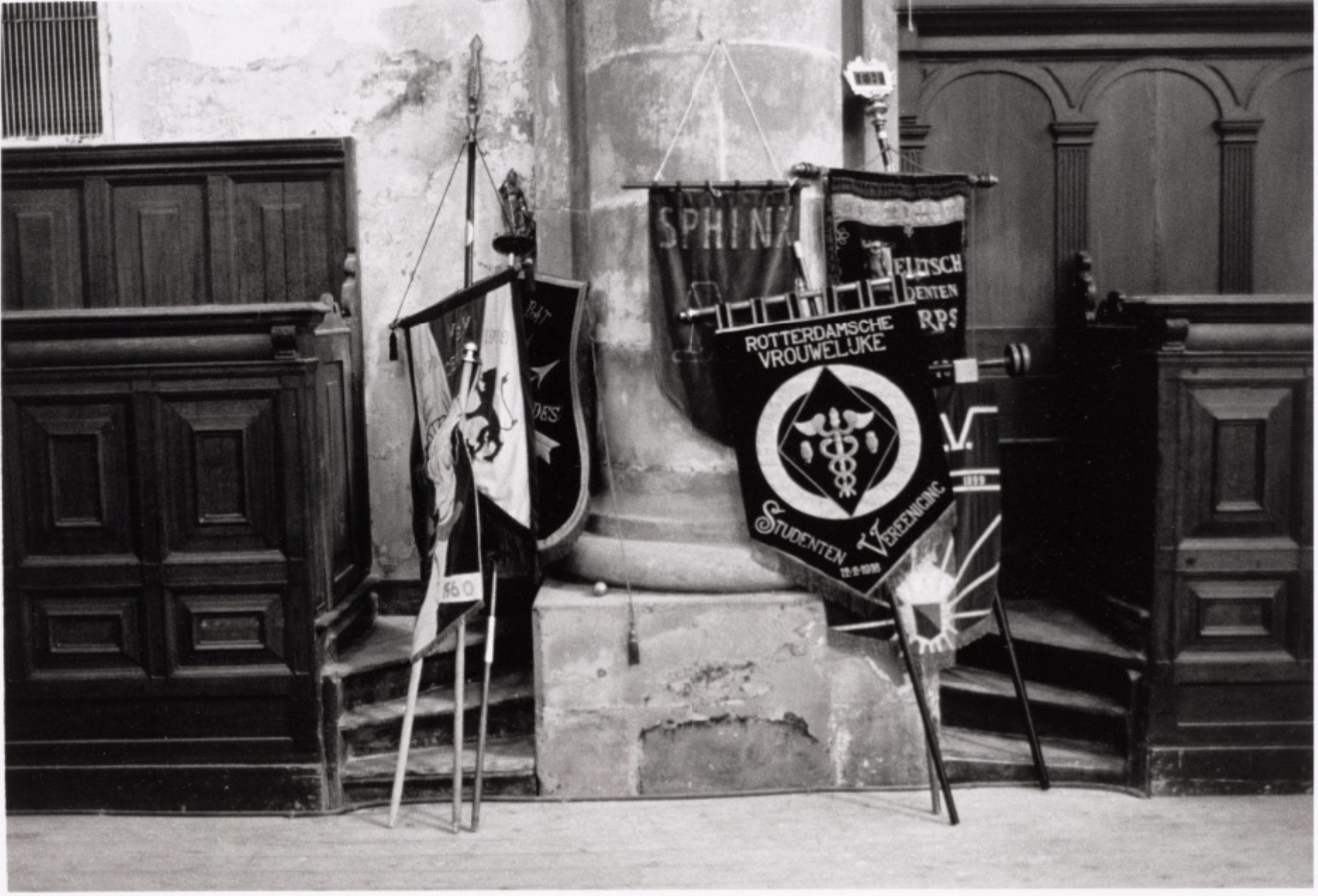 Historische zwart-witfoto van vaandels van studentenverenigingen, waaronder de Rotterdamsche Vrouwelijke Studenten Vereeniging, Sphinx en het Delftsch Studenten Corps, opgesteld in een kerk
