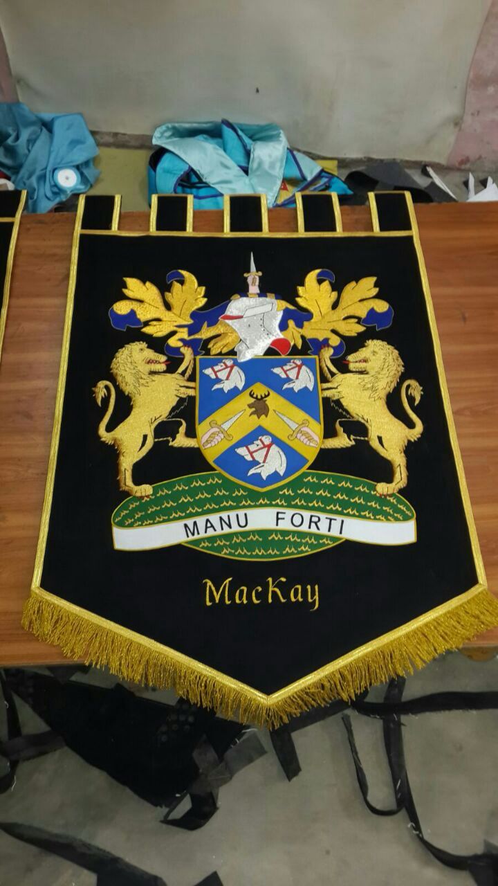 Handgeborduurd familiewapen Clan MacKay met heraldische leeuwen, helm en motto Manu Forti, op zwart fluweel met gouden franje